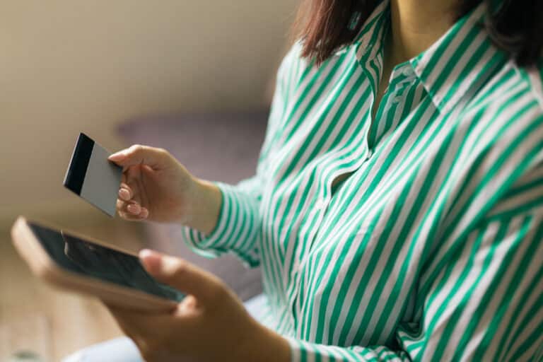 Young woman wearing a striped shirt holding a smartphone and a credit card, symbolizing e-commerce, online payment, and digital shopping processes in modern retail and banking