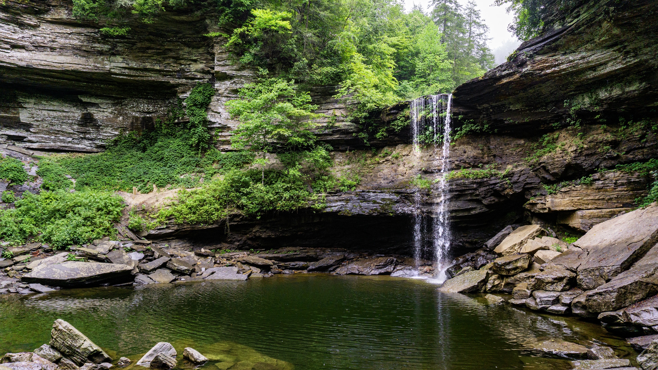 A popular swimming hole surrounded by rock cliffs and lush green foliage is below Greeter Falls in South Cumberland State Park, Tennessee.